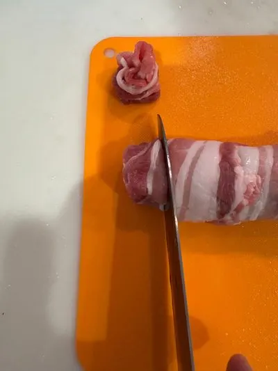 棒状の豚バラ肉を包丁で輪切りにする